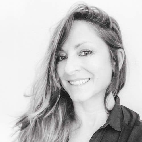 Smiling woman with long wavy hair wearing a dark shirt, in a black-and-white portrait.